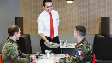 A sodexo employee handing a plate uniform to military customers