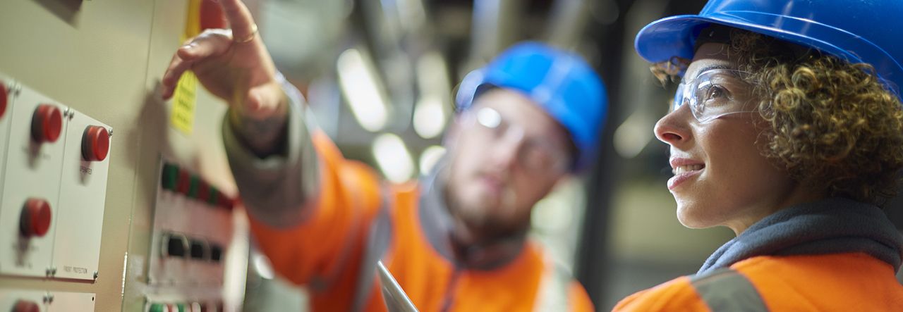 Two people wearing hard hats pointing towards the top of a machine