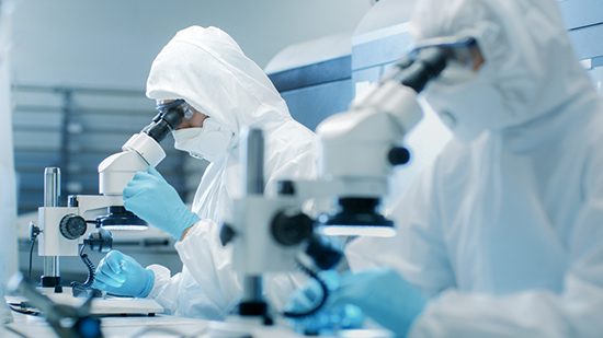 Scientists in full body protective suits looking in to microscopes